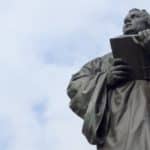 man holding book statue under white clouds during daytime