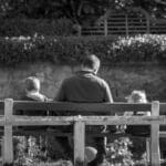 grayscale photography of man and two children sitting in bench